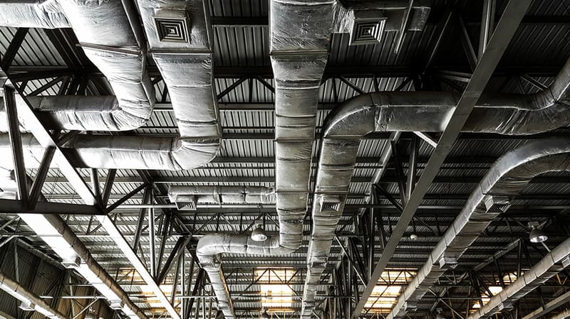 Insulated HVAC ductwork suspended from an industrial ceiling